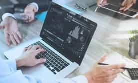 business documents on office table with smart phone and laptop computer and graph financial with social network diagram and three colleagues discussing data in the background